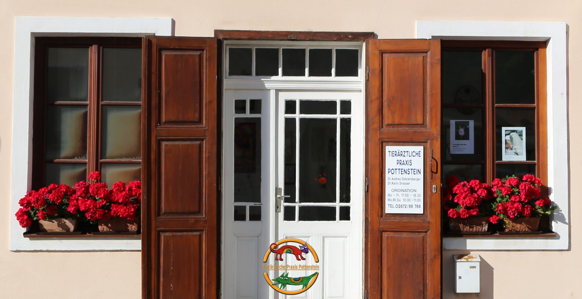 Eingang der Tierärztlichen Praxis Pottenstein mit geöffneten Fensterläden und blühenden Geranien